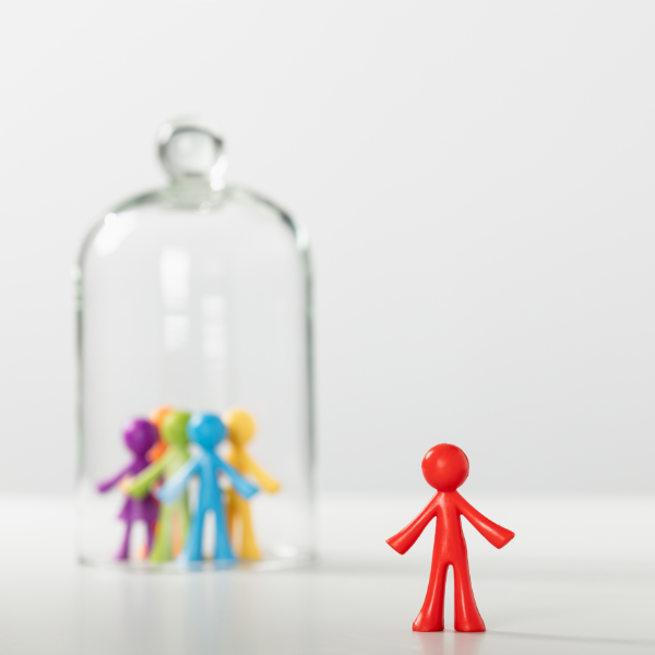 Red plastic toy figure standing away from a group of multicolour toy plastic figures all gathered under a glass jar.
